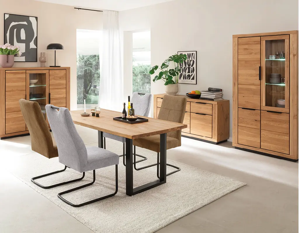 Helles Esszimmer mit massivem Esstisch aus Eiche und komfortablen Stühlen mit schwarzem Metallgestell. Moderne Holzkommoden und dekorative Accessoires schaffen eine warme und stilvolle Atmosphäre.